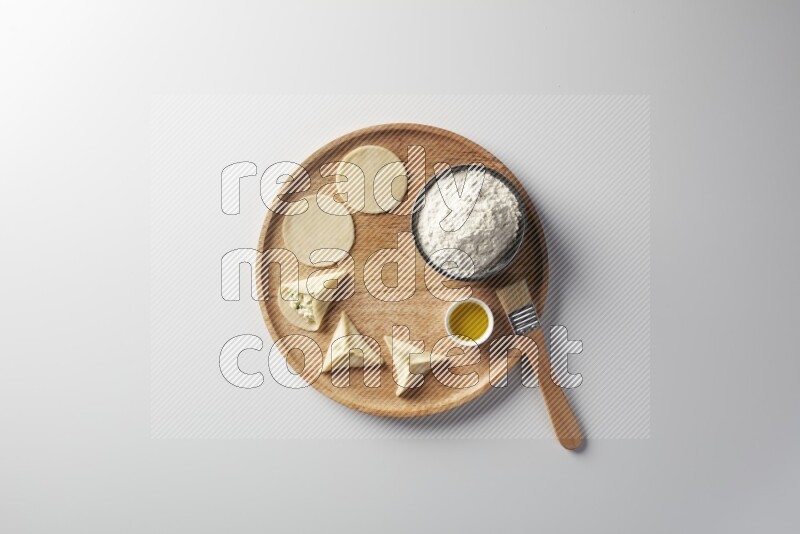 two closed sambosas and one open sambosa filled with cheese while flour, and oil with oil brush aside in a wooden dish on a white background