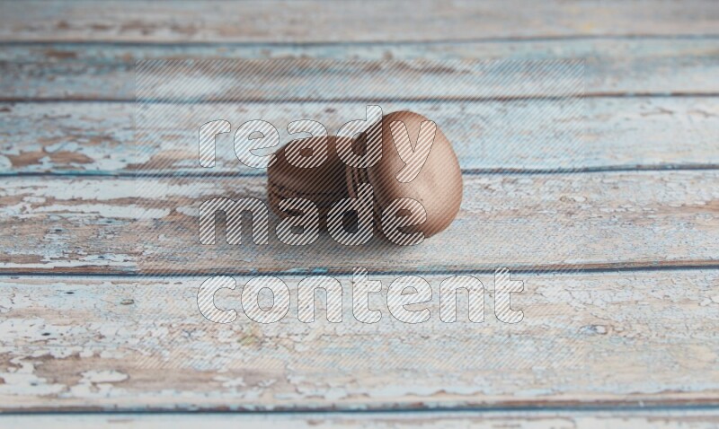 45º Shot of two Brown Dark Chocolate macarons on light blue wooden background