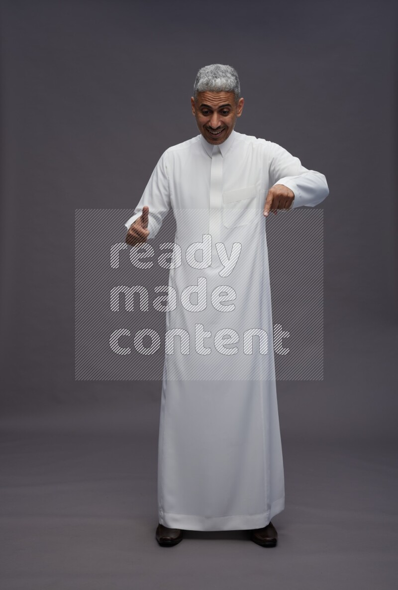 Saudi man wearing thob standing interacting with the camera on gray background