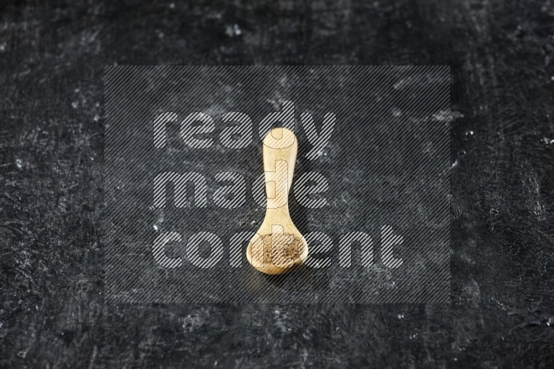 ملعقة خشبية ممتلئة ببودرة الكمون على خلفية سوداء