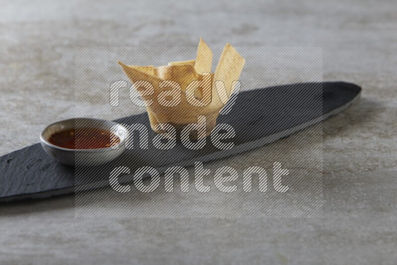 wonton cups with soy sauce ramkin on oval slate on grey textured counter top