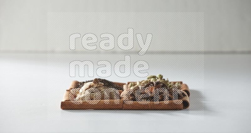 4 مربعات من أعواد القرفة ممتلئة بالشاي والهيل واليانسون والزنجبيل على أرضية بيضاء