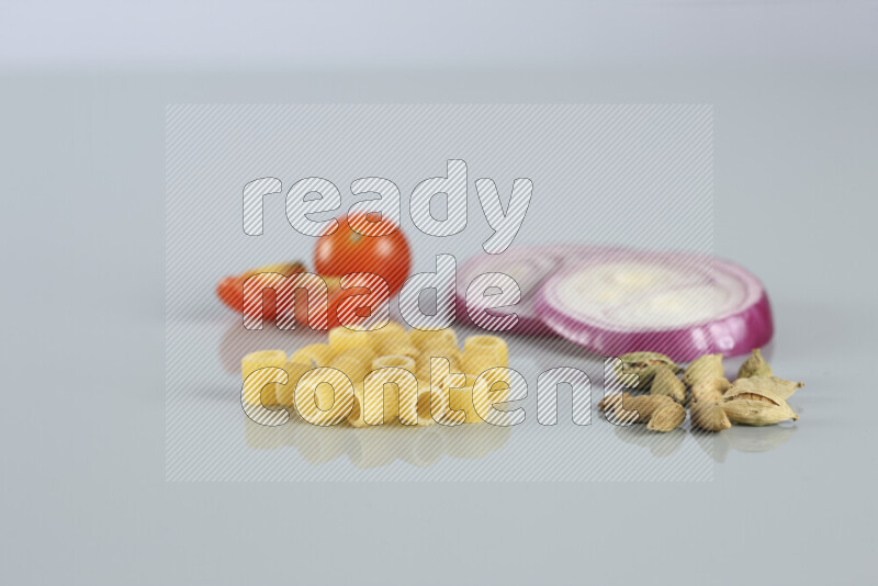Raw pasta with different ingredients such as cherry tomatoes, garlic, onions, red chilis, black pepper, white pepper, bay laurel leaves, rosemary, cardamom and mushrooms on light blue background