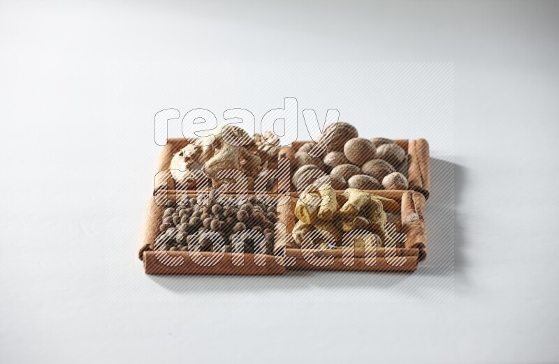 4 مربعات من أعواد القرفة ممتلئة بجوزة الطيب والزنجبيل المجفف وأصابع الكركم وبهار الفلفل الحلو على أرضية بيضاء