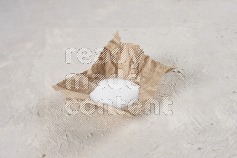 A crumpled piece of paper full of white salt on white background