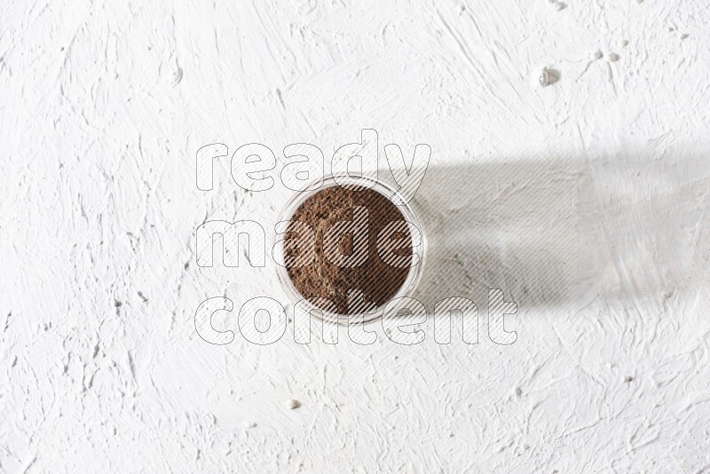 A glass jar full of cloves powder on a textured white flooring
