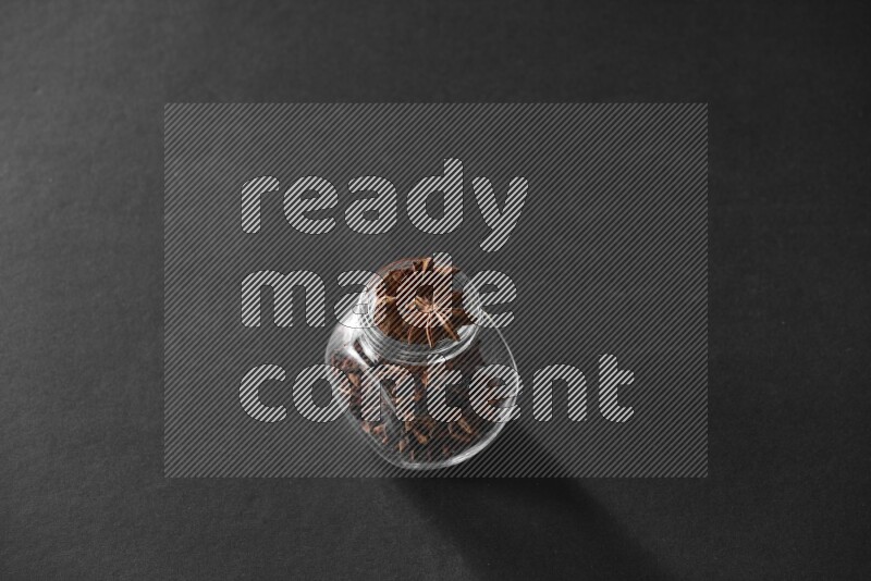 A glass spice jar full of star anise on black flooring