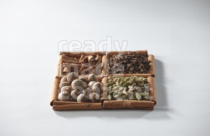 4 مربعات من أعواد القرفة ممتلئة بالهيل والقرفة والقرنفل وجوزة الطيب على أرضية بيضاء