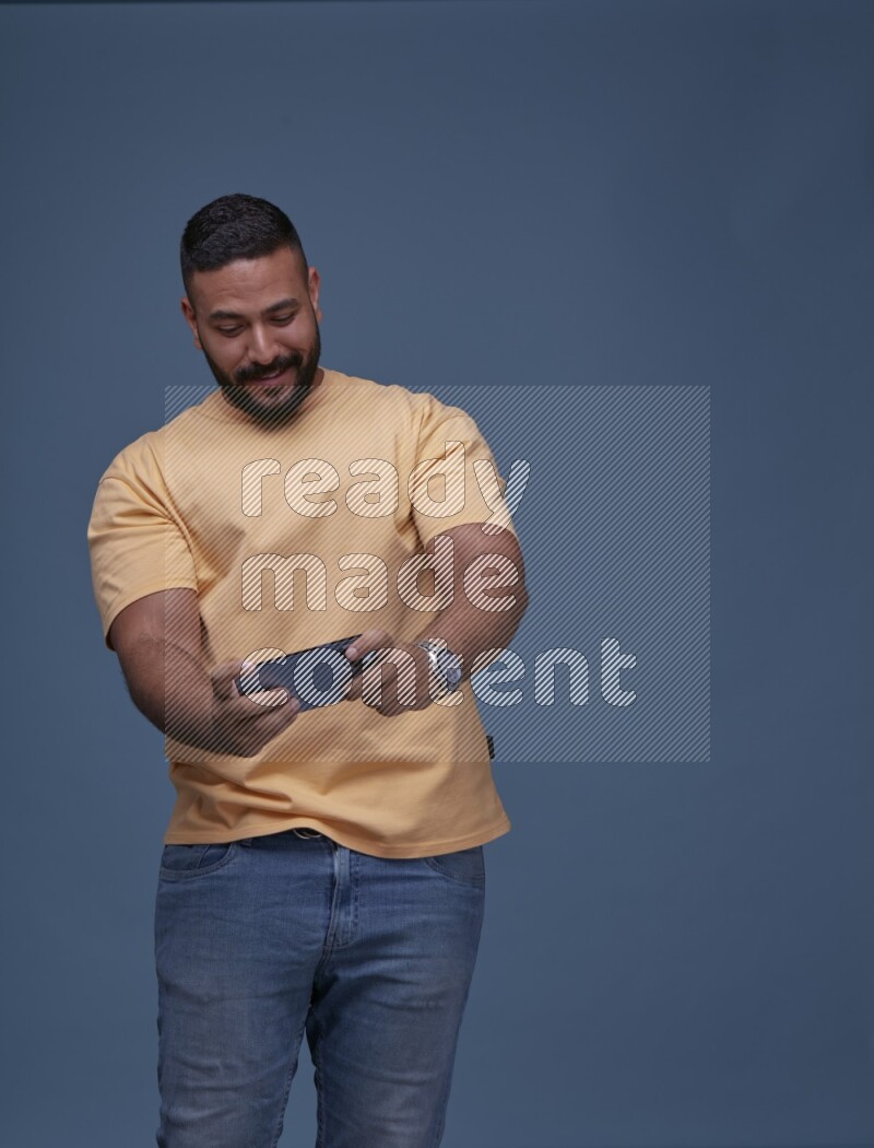 A man Playing Games on Smartphone on Blue Background wearing Orange T-shirt