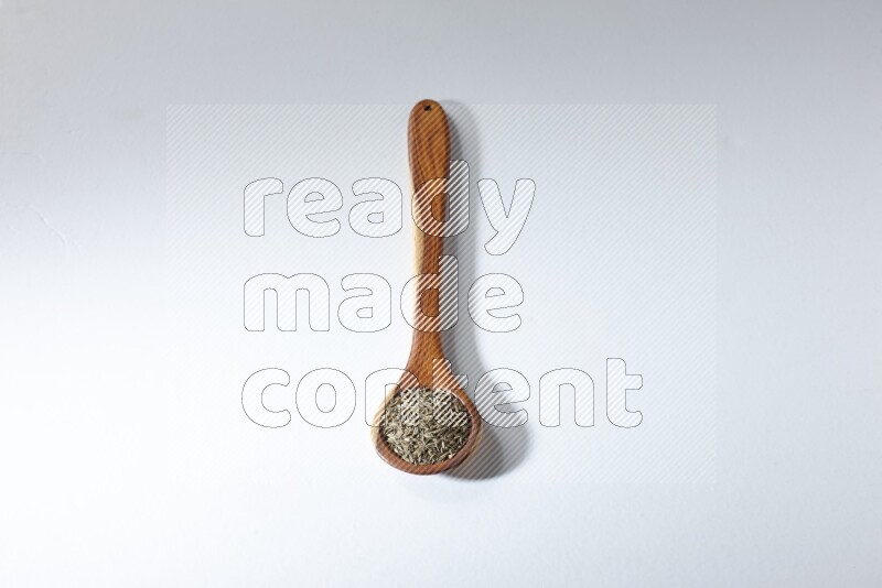 A wooden ladle full of cumin seeds on a white flooring
