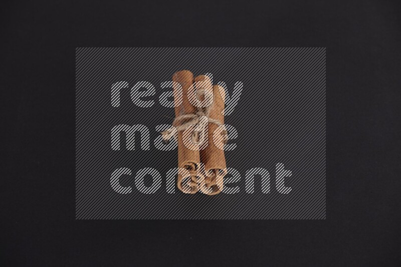 4 أعواد من القرفة مربوطة علي خلفية سوداء