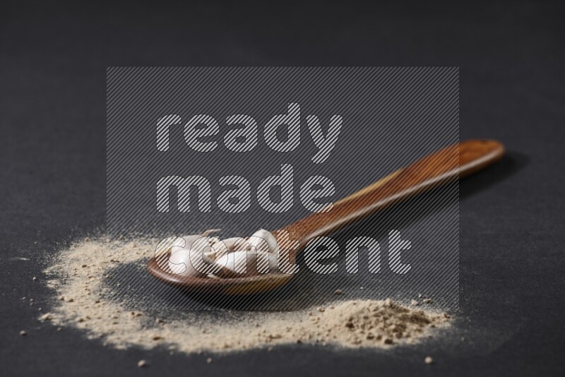 A wooden ladle full of garlic cloves with sprinkled powder on a black flooring