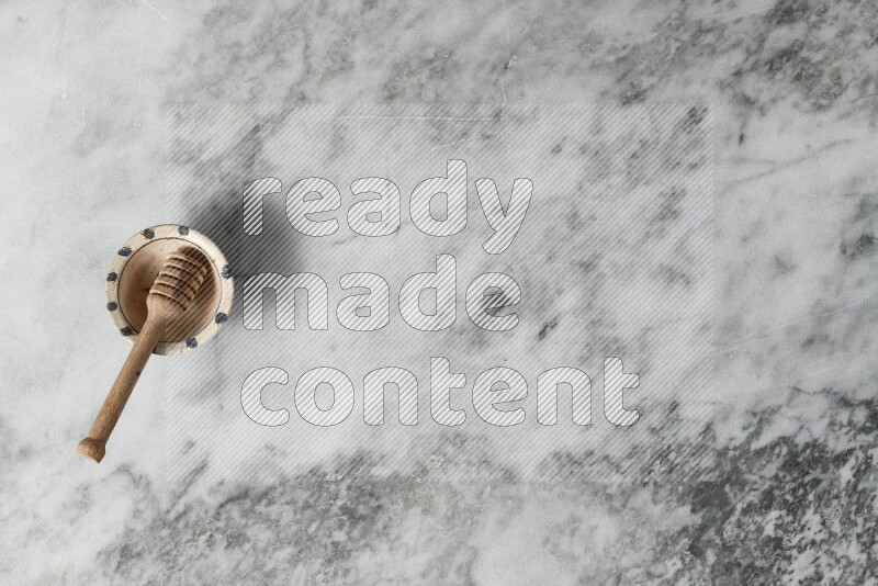 وعاء فخاري مزخرف مع ملعقة عسل خشبية بداخله على خلفية من الرخام الرمادي