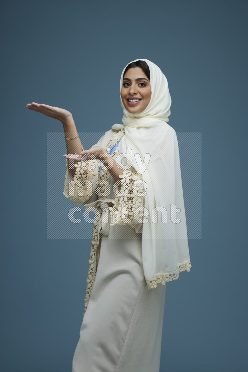 A Saudi woman pointing in a blue background wearing an off-white Abaya Hijab