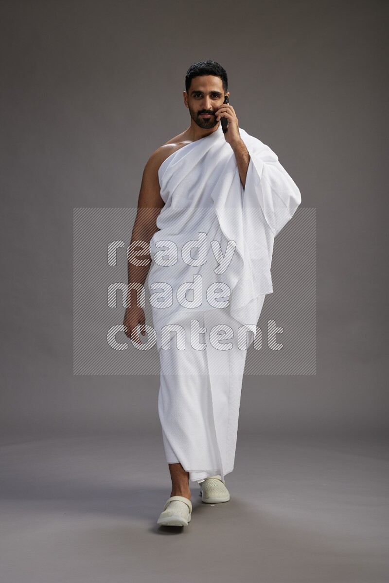 A man wearing Ehram Standing talking on phone on gray background