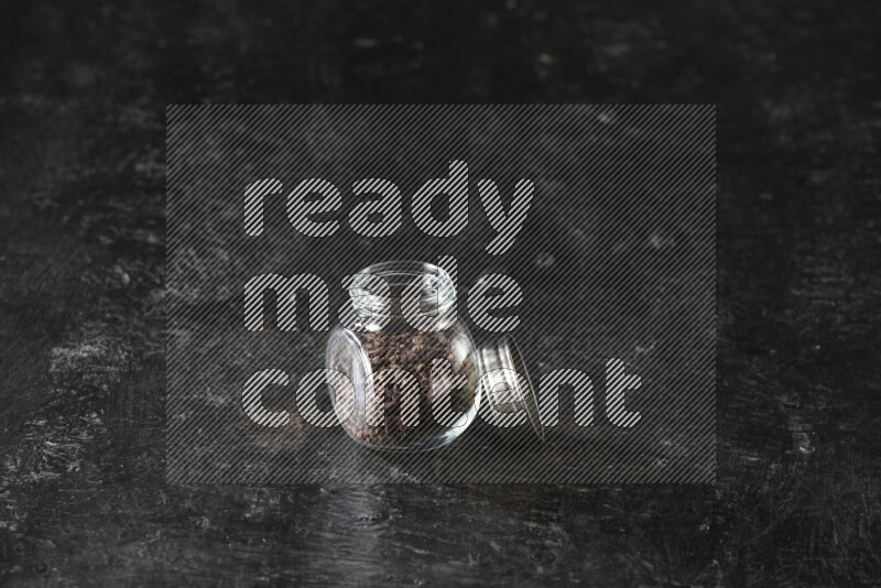 A glass spice jar full of cloves on textured black flooring