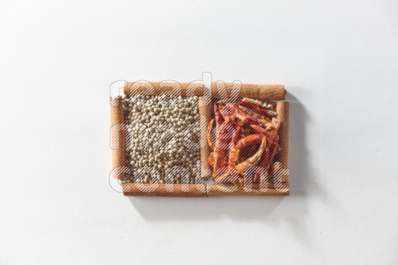 مربعان من أعواد القرفة ممتلئان بالفلفل الحار المجفف وحبوب الفلفل الأبيض علي خلفية بيضاء