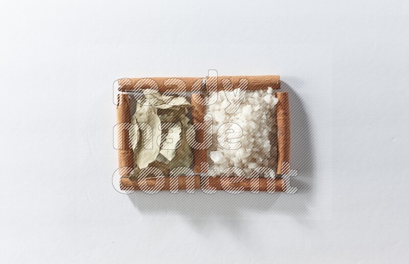 مربعان من أعواد القرفة ممتلئان بالملح الأبيض وأوراق الغار علي خلفية بيضاء