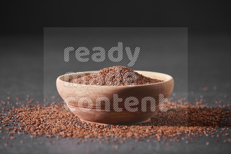 وعاء خشبي ممتلئ ببذور حب الرشاد محاط ببعض البذور علي خلفية سوداء