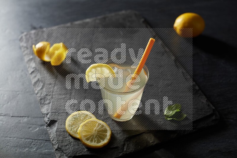 A glass of lemon juice with a straw on black background