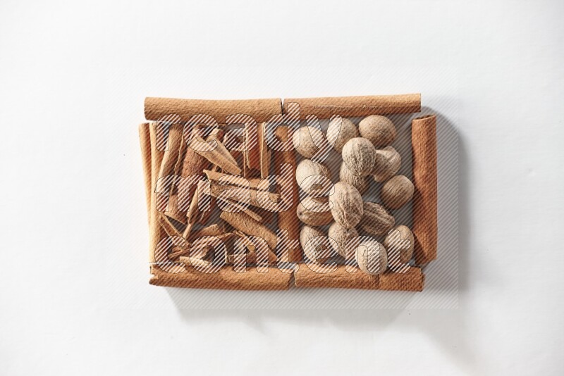 مربعان من أعواد القرفة ممتلئان بقطع من القرفة وجوزة الطيب علي خلفية بيضاء