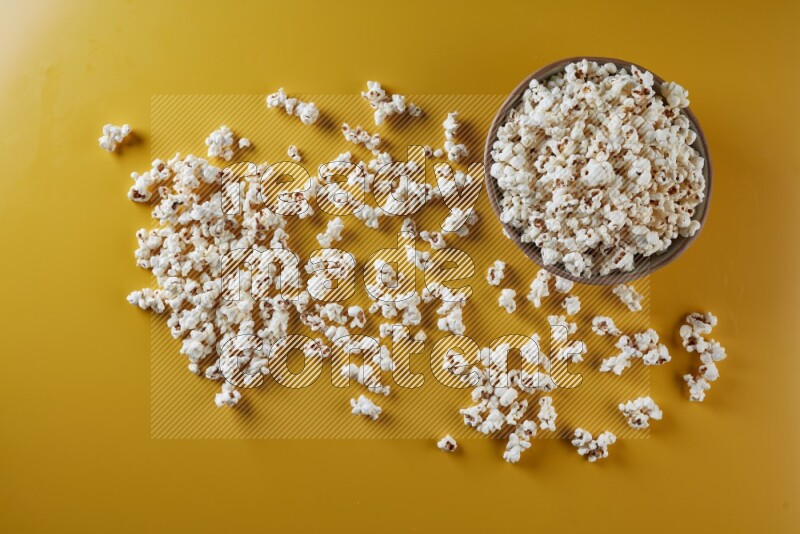 A brown pottery bowl full of popcorn with popcorn beside it on a yellow background in different angles