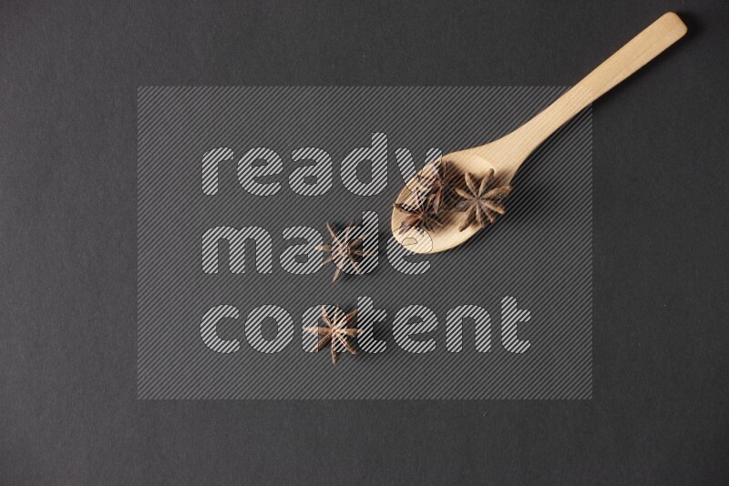 اليانسون النجمي في ملعقة خشبية فوق اليانسون النجمي الذي يغطي الإطار على أرضية سوداء