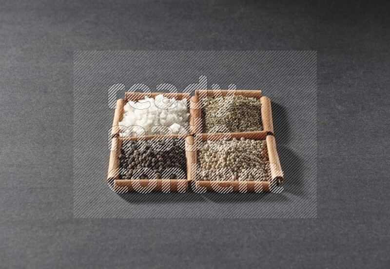 4 مربعات من عيدان القرفة ممتلئة بحبوب الفلفل الأسود والكمون وحبوب الفلفل الأبيض والملح الأبيض على أرضية سوداء