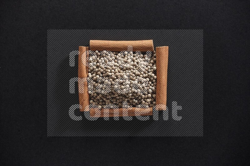 A single square of cinnamon sticks full of white pepper on black flooring