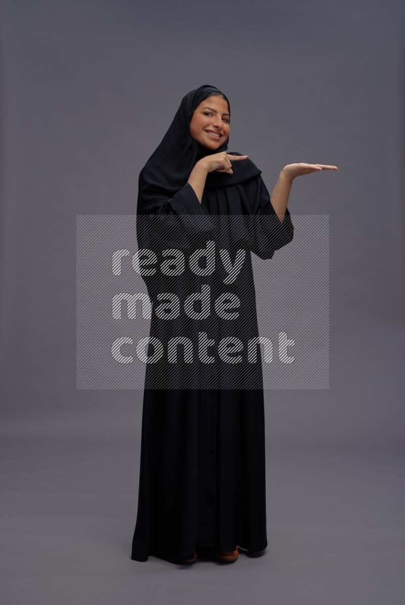 Saudi woman wearing Abaya standing interacting with the camera on gray background
