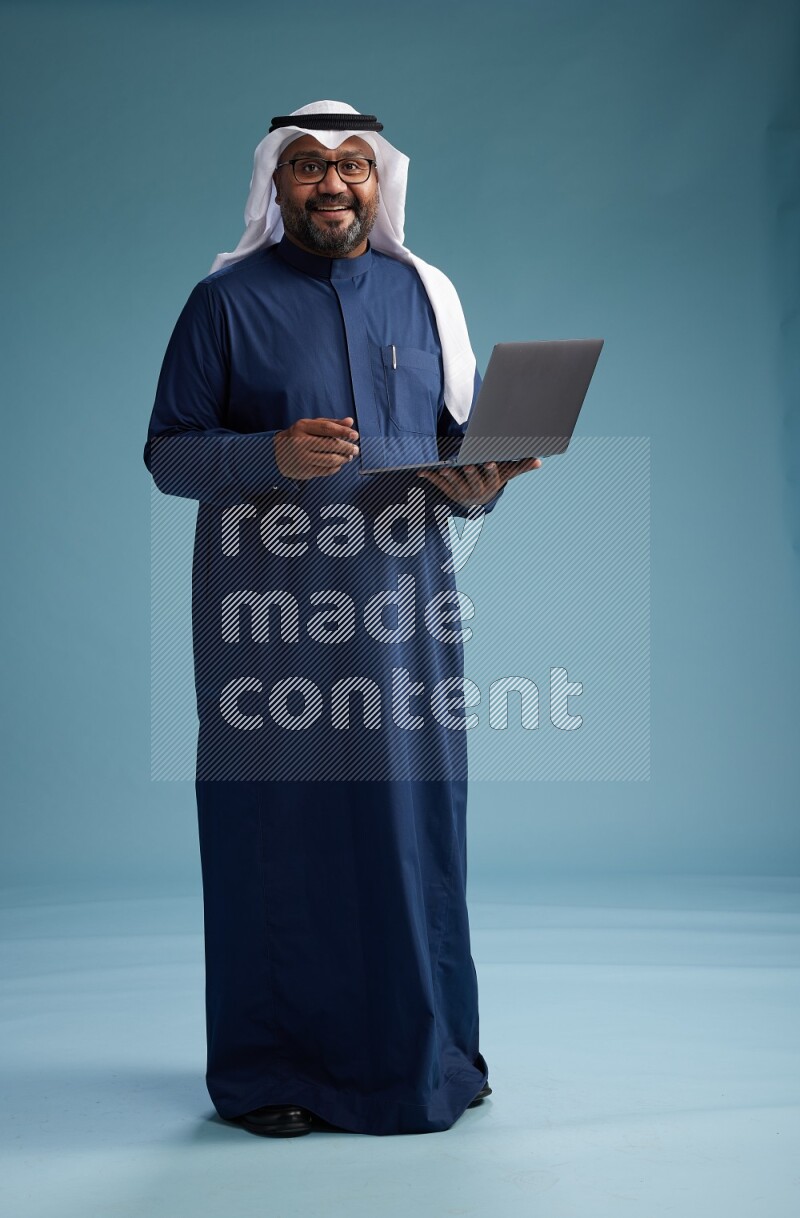 Saudi Man with shimag Standing working on laptop on blue background