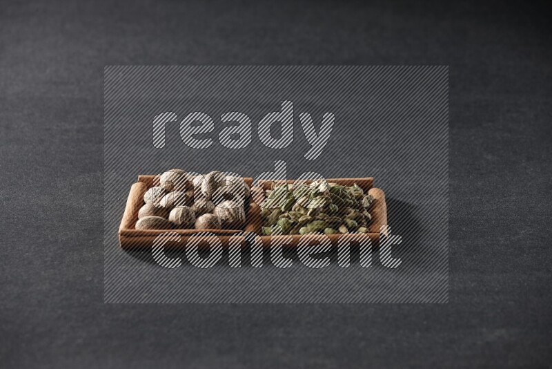 مربعان من أعواد القرفة ممتلئان بجوزة الطيب وحبوب الهيل علي خلفية سوداء