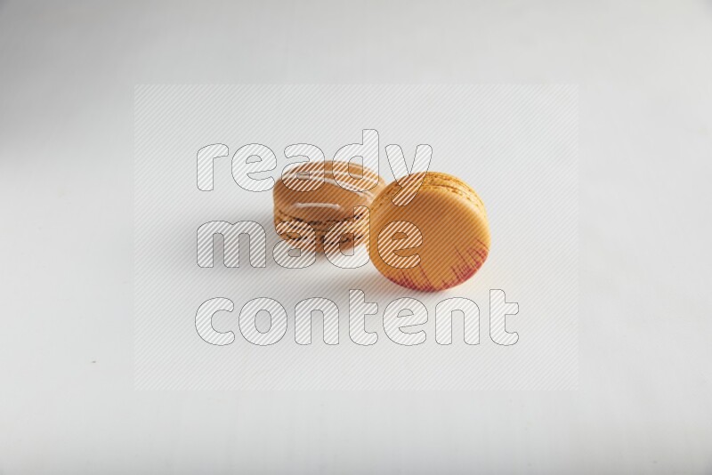 45º Shot of of two assorted Brown Irish Cream, and Orange Exotic macarons on white background