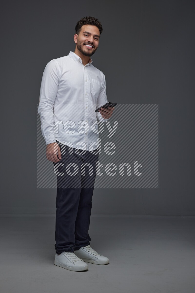 A man wearing smart casual standing and using his phone eye level on a gray background