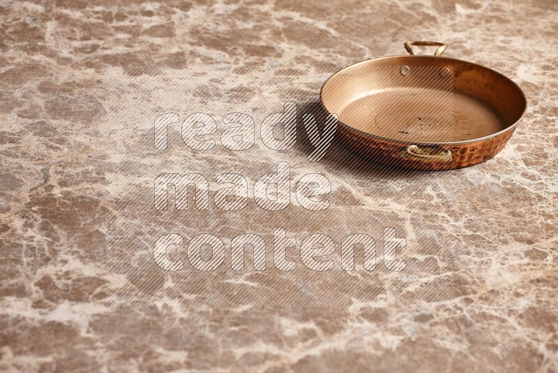 A small copper pan on beige marble background