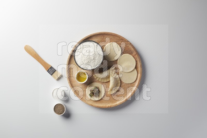 two closed sambosas and one open sambosa filled with meat while flour, salt, black pepper and oil with oil brush aside in a wooden dish on a white background