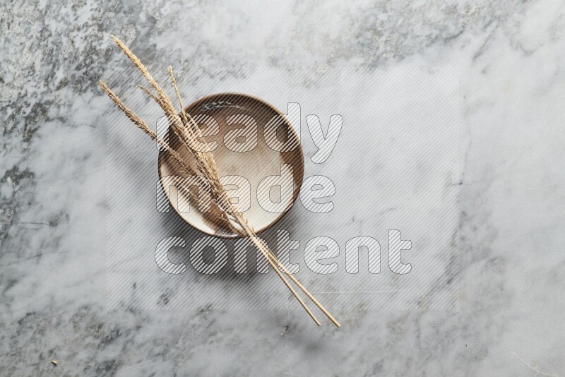 Wheat stalks on multicolored pottery plate on grey marble background