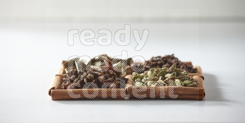 4 مربعات من أعواد القرفة ممتلئة بالهيل واليانسون والقرنفل وأوراق الغار على أرضية بيضاء