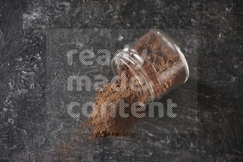 A flipped glass jar full of cloves powder on a textured black flooring