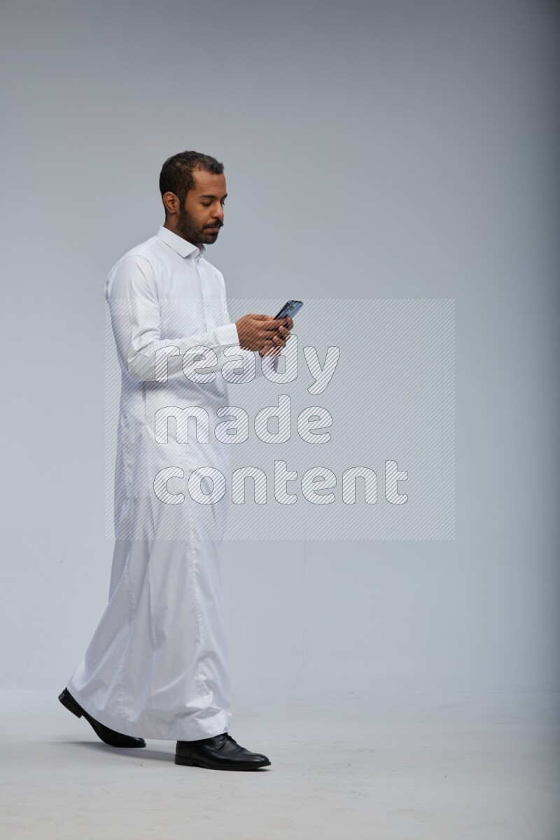 Saudi man wearing Thob standing texting on phone on Gray background