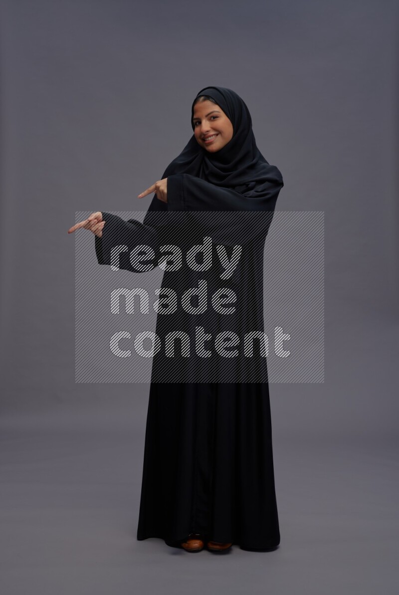 Saudi woman wearing Abaya standing interacting with the camera on gray background