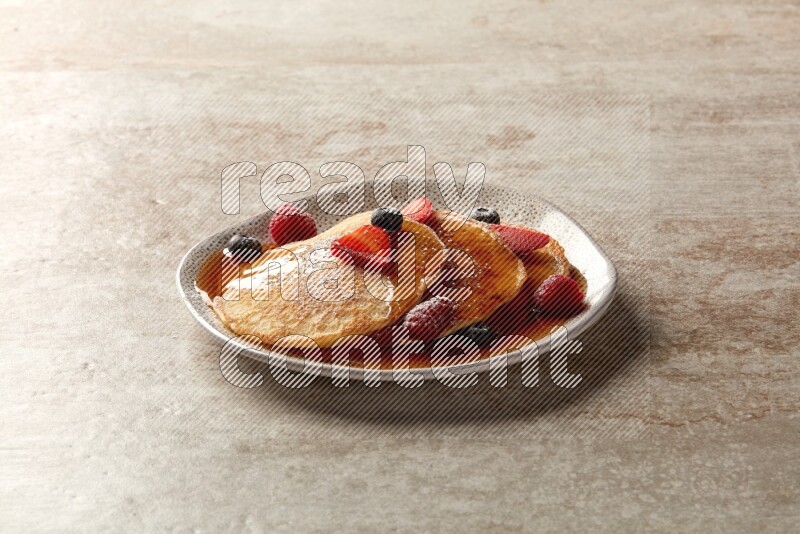 Three stacked mixed berries pancakes in an irregular plate on beige background