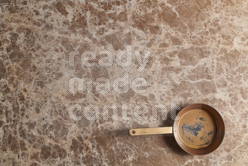 A small copper pan on beige marble background