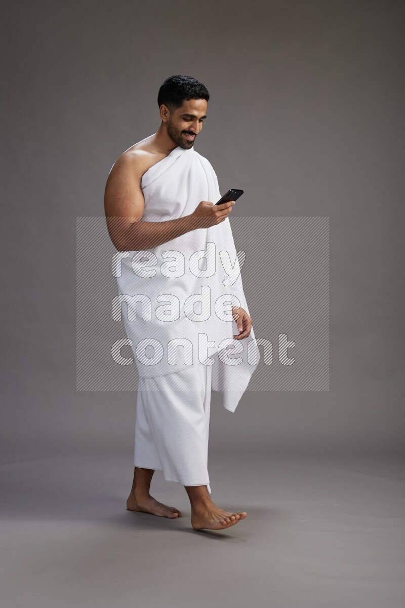 A man wearing Ehram Standing texting on phone on gray background