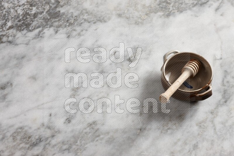 وعاء فخاري متعدد الألوان مع ملعقة عسل خشبية بداخله على خلفية من الرخام الرمادي