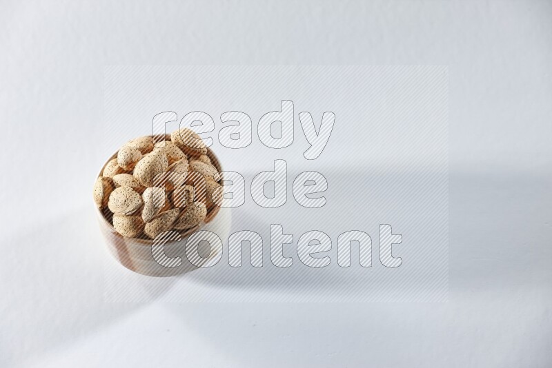 A beige ceramic bowl full of almonds on a white background in different angles
