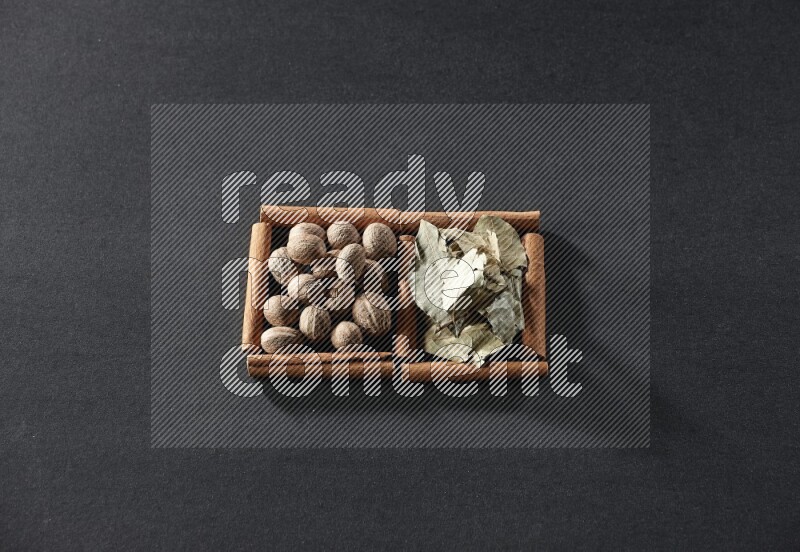 مربعان من أعواد القرفة ممتلئان بجوزة الطيب وأوراق الغار علي خلفية سوداء