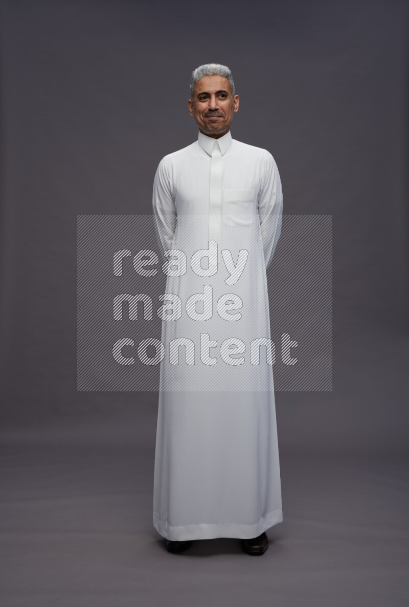 Saudi man wearing thob standing interacting with the camera on gray background