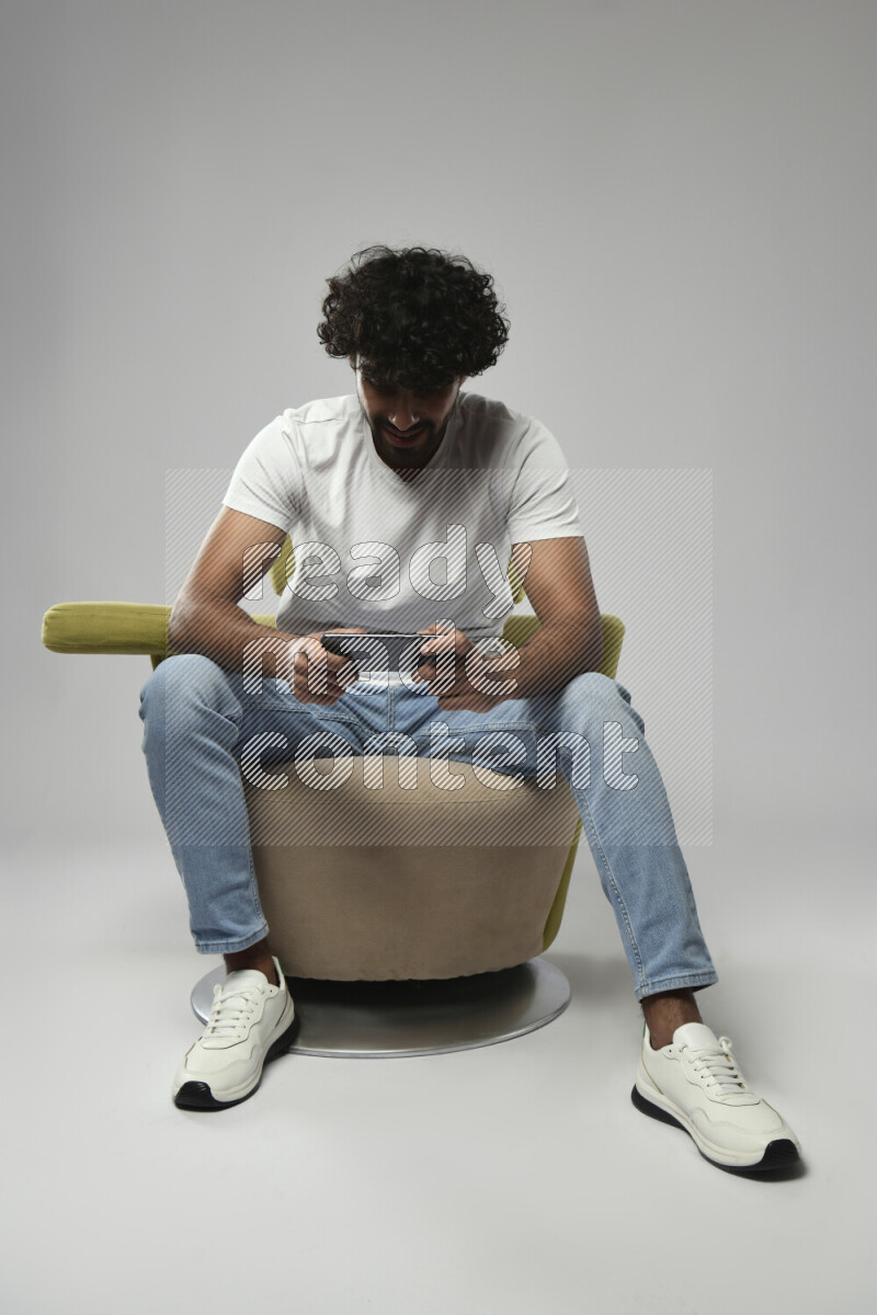 A man wearing casual sitting on a chair gaming on the phone on white background