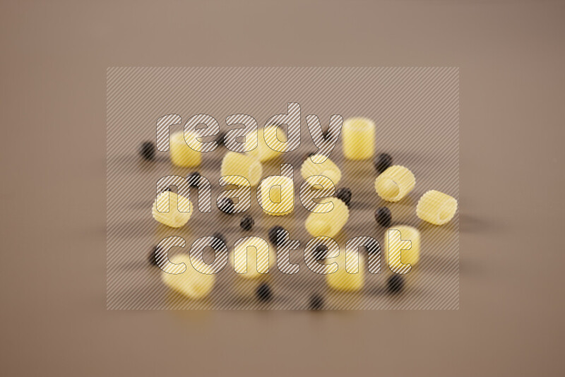 Raw pasta with different ingredients such as cherry tomatoes, garlic, onions, red chilis, black pepper, white pepper, bay laurel leaves, rosemary and cardamom on beige background